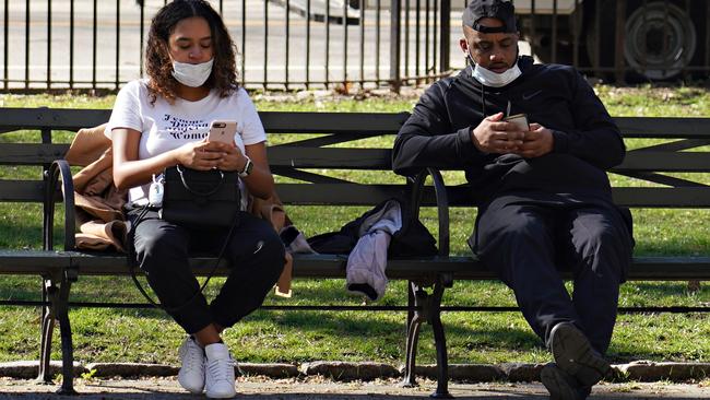 Two people, on a bench in New York, with protective masks use their phones. Picture: Getty Images