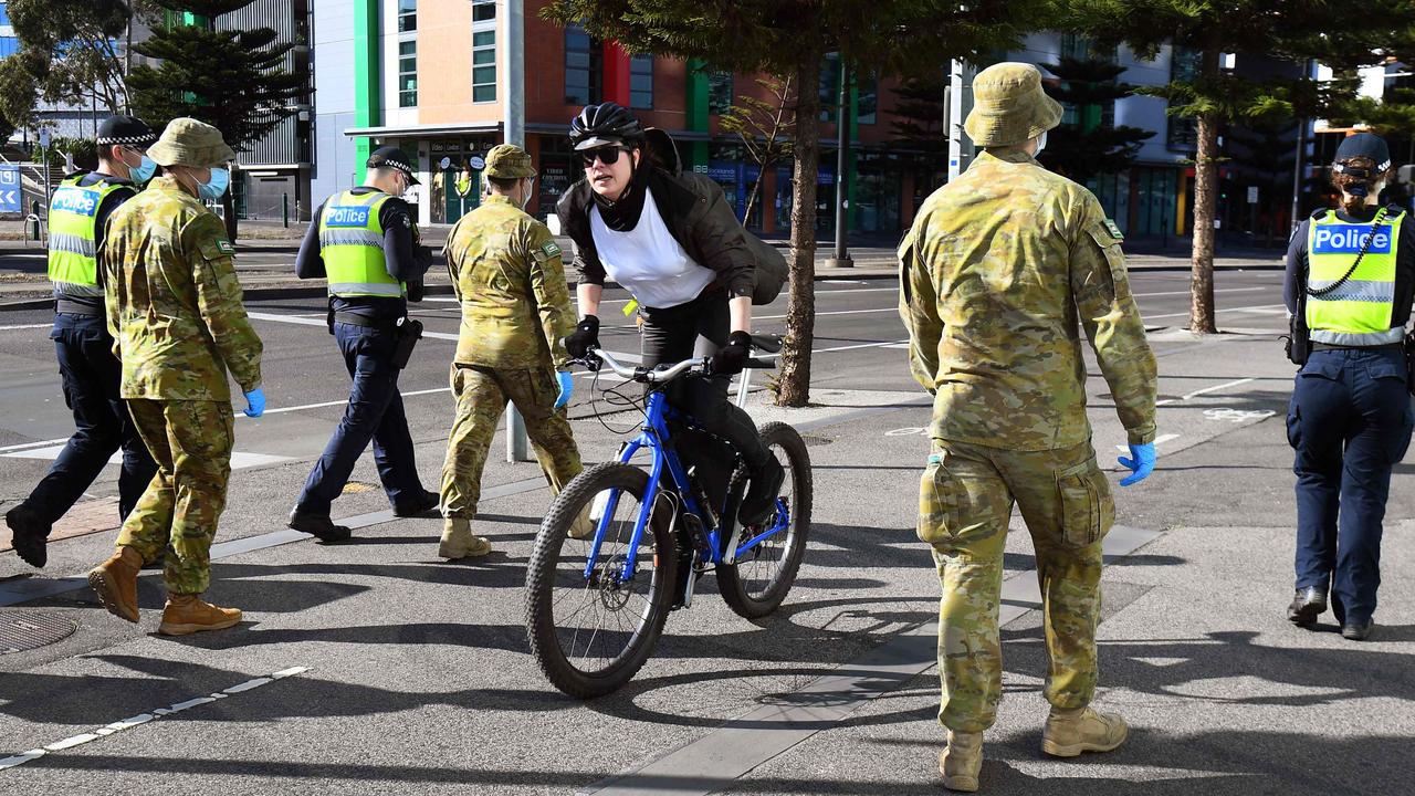 A cyclist passes a group of police and soldiers patrolling the Docklands area of Melbourne on Sunday. Picture: William West/AFP