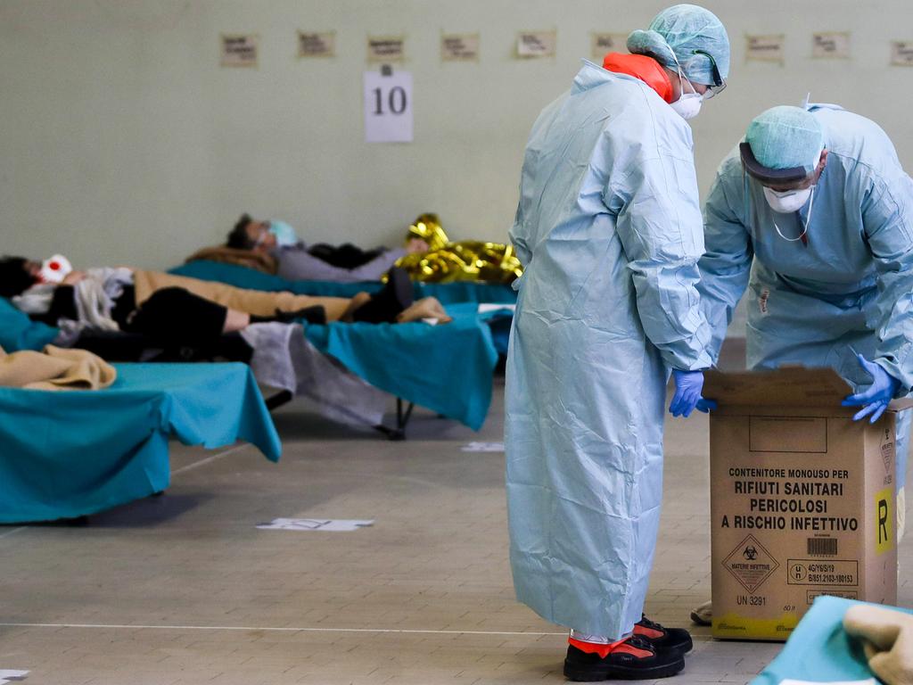 Paramedics carry a hazardous medical waste box as patients lie on camp beds in one of the emergency structures that were set up to ease procedures at the Brescia hospital, northern Italy. Picture: Luca Bruno/AP