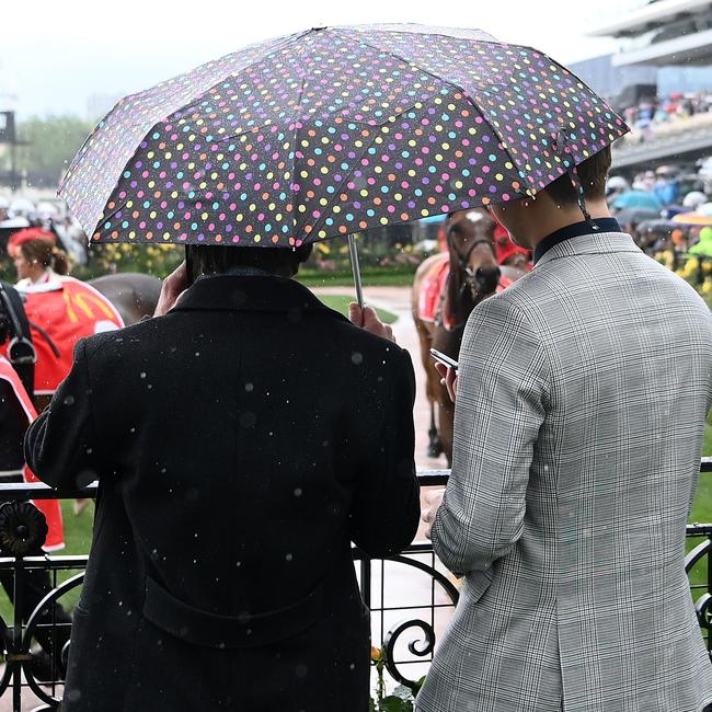 Rain falls as spectators watch horses in the mounting yard.