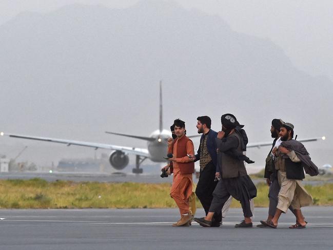 Taliban fighters walk past a Qatar Airways aircraft preparing to take off from the airport in Kabul in September. It has been one of the few airlines with permission from the Taliban to operate evacuation flights and takes passengers to a US-run processing centre in Doha. Picture: Wakil Kohsar/AFP