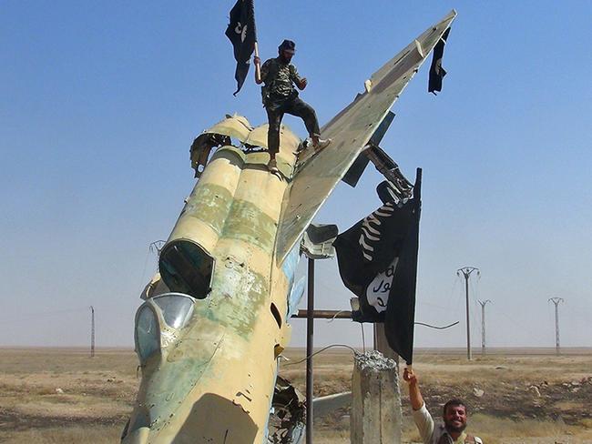 Taking over ... fighters of the Islamic State wave the group's flag from a damaged display of a government fighter jet following the battle for the Tabqa air base, in Raqqa, Syria. Picture: AP Photo/Raqqa Media Center of the Islamic State group