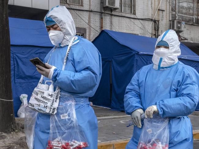 BEIJING, CHINA - NOVEMBER 30: Epidemic control workers wear PPE to prevent the spread of COVID-19 as they walk carrying bags of nucleic acid tests while working in an area with communities under lockdown on November 30, 2022 in Beijing, China. In recent days, China has been recording its highest number of COVID-19 cases since the pandemic began, as authorities are sticking to their strict zero tolerance approach to containing the virus with lockdowns, mandatory testing, mask mandates, and quarantines as it struggles to contain outbreaks.In an effort to try to bring rising cases under control, the government last week closed most stores and restaurants for inside dining, switched  schools to online studies, and told people to work from home among other measures. (Photo by Kevin Frayer/Getty Images)