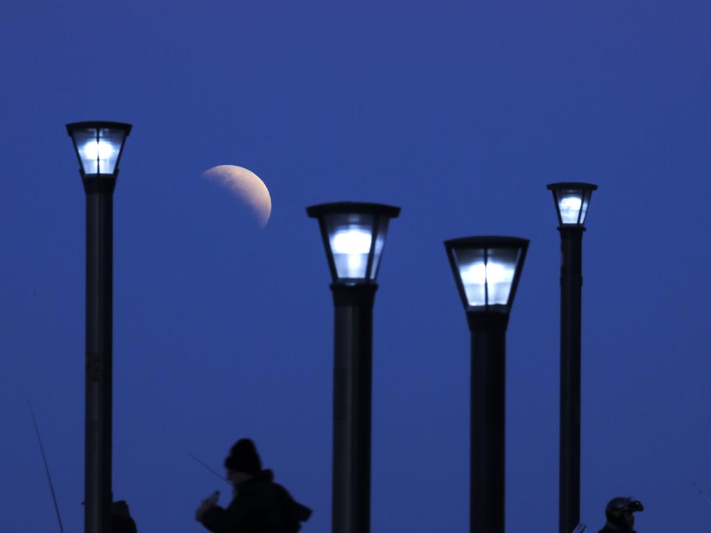 Men stand below street lights as the moon rises during a partial lunar eclipse in Buenos Aires, Argentina, Tuesday, July 16, 2019. (AP Photo/Natacha Pisarenko)