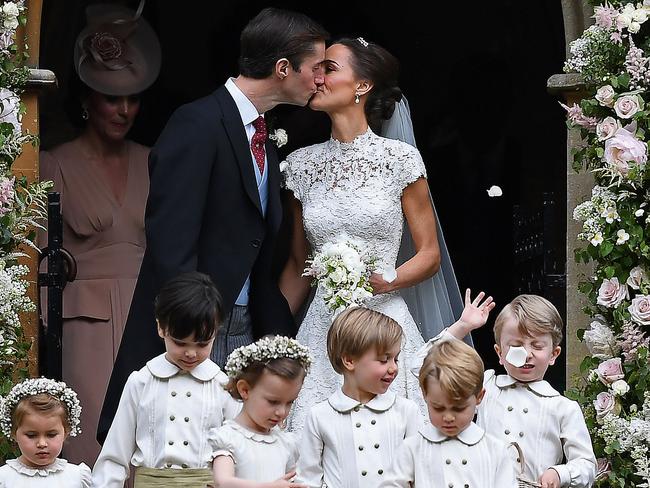 TOPSHOT - Pippa Middleton (R) kisses her new husband James Matthews, following their wedding ceremony at St Mark's Church in Englefield, west of London, on May 20, 2017, as the bridesmaids, including Britain's princess Charlotte (L) and pageboys, including Britain's prince George (2R), walk ahead. After turning heads at her sister Kate's wedding to Prince William, Pippa Middleton graduated from bridesmaid to bride on Saturday at a star-studded wedding in an English country church. The 33-year-old married financier James Matthews, 41, at a ceremony attended by the royal couple and tennis star Roger Federer, wearing a couture dress by British designer Giles Deacon.  / AFP PHOTO / POOL / Justin TALLIS