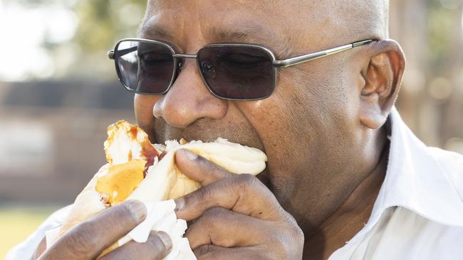 The things you do for work: Lawrence Machado enjoying his sausage sizzle at Panania Public School. Picture: Matthew Vasilescu