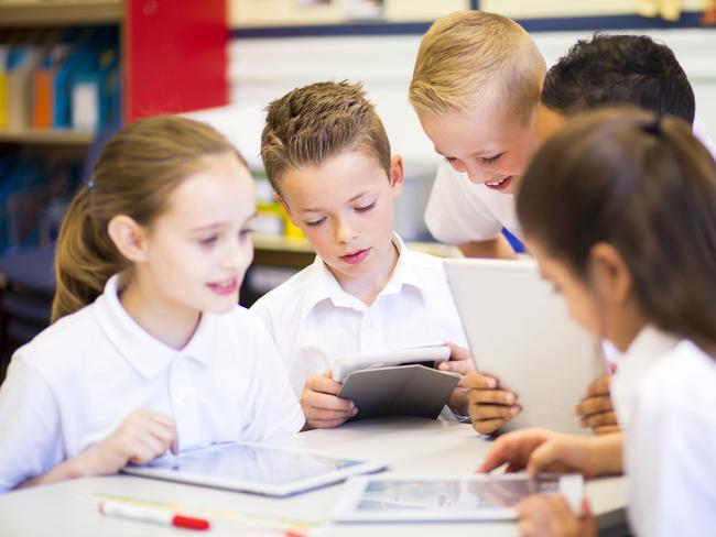 Happy students in classroom using a digital tablet, they are all wearing uniforms.