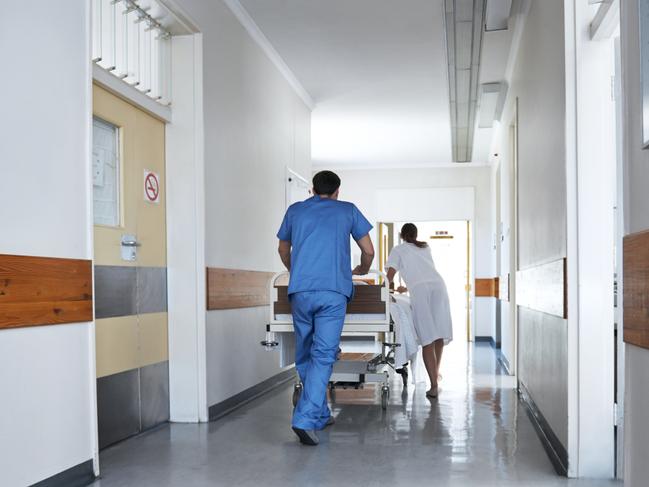 Rearview shot of hospital staff wheeling a patient in a gurney down a corridor