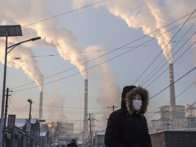 SHANXI, CHINA -NOVEMBER 26: (CHINA, HONG KONG, MACAU, TAIWAN OUT) Smoke billows from stacks as a Chinese woman wears as mask while walking in a neighborhood next to a coal fired power plant on November 26, 2015 in Shanxi, China. A history of heavy dependence on burning coal for energy has made China the source of nearly a third of the world's total carbon dioxide (CO2) emissions, the toxic pollutants widely cited by scientists and environmentalists as the primary cause of global warming. China's government has publicly set 2030 as a deadline to reach the country's emissions peak, and data suggest the country's coal consumption is already in decline. The governments of more than 190 countries are expected to sign an agreement in Paris to set targets on reducing carbon emissions in an attempt to forge a new global agreement on climate change.  (Photo by Kevin Frayer/Getty Images)