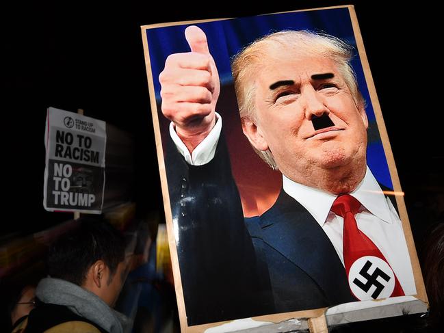 TOPSHOT - A demonstrator holds a placard showing a picture of US President-elect Donald Trump modified to add a swastika and an Adolf Hitler-style moustache during a protest outside the US Embassy in London November 9, 2016 against Trump after he was declared the winner of the US presidential election.  Political novice and former reality TV star Donald Trump has defeated Hillary Clinton to take the US presidency, stunning America and the world in an explosive upset fueled by a wave of grassroots anger. / AFP PHOTO / BEN STANSALL