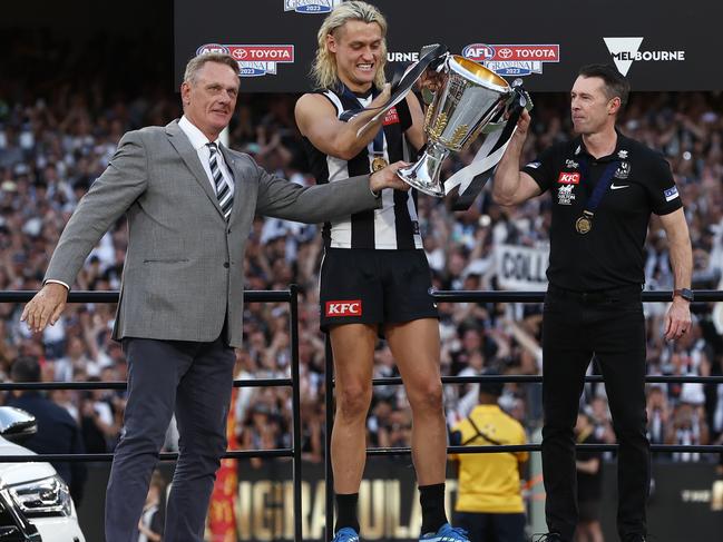 Collingwood captain Darcy Moore, centre, and coach Craig McRae receive the premiership cup from Darcy’s father Peter Moore (far left). Picture: Michael Klein