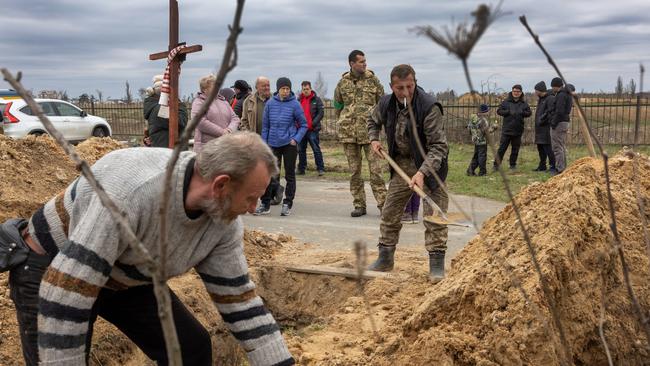 Ukrainian grave diggers shovel soil into an open grave after the Bucha massacre. Picture: AFP.