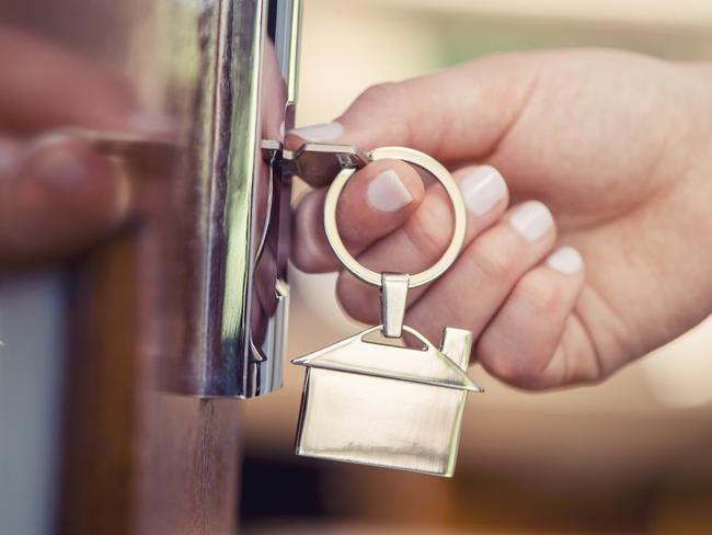 Woman using a house key on the front door. Close up of he woman??s hand. She is turning the key in the lock. There is a hallway in the  background. The key ring has a house icon on it.