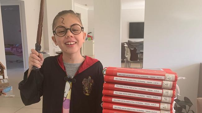 Eight-year-old Eva in her Hogwarts robe alongside the Harry Potter series written in Braille.