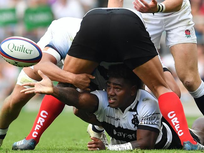 Fijian wing Josua Tuisova (C) passes the ball from the floor during the match between England and the Barbarians at Twickenham.