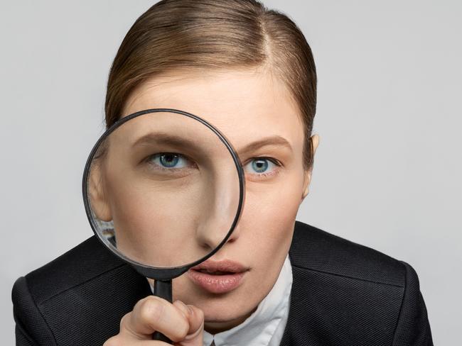 Portrait of a girl in the office at work looks carefully into the magnifying glass with one eye. The concept of office work and search. tax generic