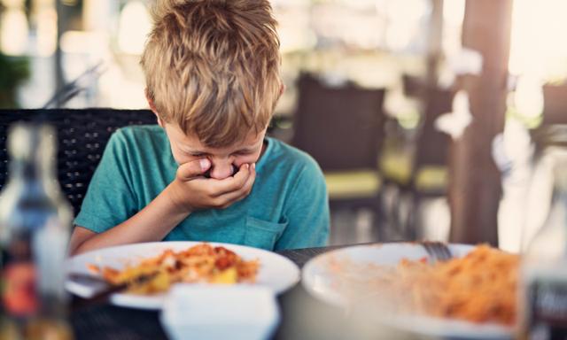 Little boy fussy eater in restaurant. The boy doesnt want to eat and he is even going to throw up even looking at his plate.