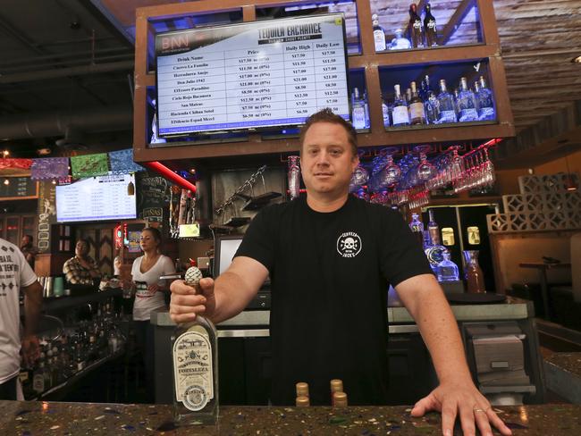 In this Thursday, May 5, 2016, photo, Frank Miller, a partner in a series of eight bars in San Diego, shows off some of the tequila collection at The Blind Burro, in San Diego, where the tequila prices can change every five minutes based on demand. The electronic Tequila Exchange board, behind and above Miller, shows the current prices for the bar's tequilas. (AP Photo/Lenny Ignelzi)