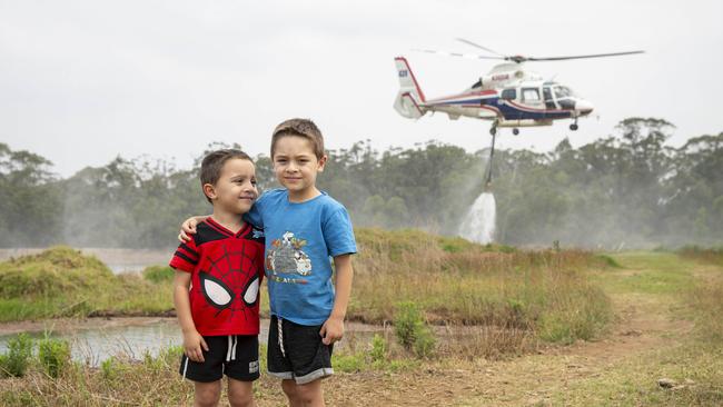 Lucas Grima, 4, and Jacob Grima, 5, in front of a RFS helicopter filling up it's tank from their grandparent’s dam to fight the fires surrounding them. Picture: Adam Yip