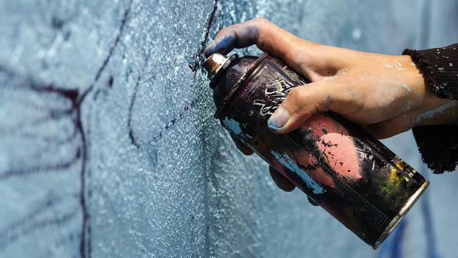 A young man holds a dark can of spray paint close to a blue wall to sketch his graffiti. iSTOCK