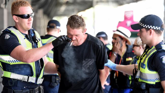 A police officer removes the cigarette to take the man to the divvy van. Picture: Nicole Garmston