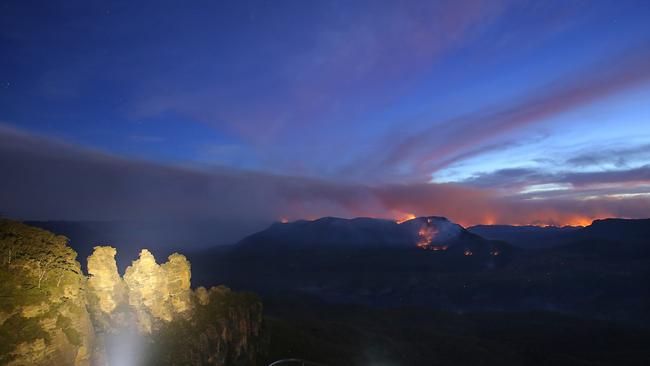 A long exposure photograph shows the Three Sisters rock formation as flames from the Kowmung River fire and the Green Wattle Creek fire are seen from Echo Point lookout in Katoomba. Picture:AAP/Steven Saphore