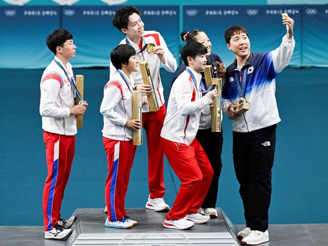 Bronze medalists South Korea's Lim Jonghoon (R) takes a selfie picture with his mobile as he celebrates on the podium with : gold medalists China's Wang Chuqin (rear 2nd L) and China's Sun Yingsha (front 2nd L), silver medalists North Korea's Ri Jong Sik (L), and North Korea's Kim Kum Yong (front 2nd L) and bronze medallist and teammate South Korea's Shin Yubin (2nd R) at the end of their mixed table tennis doubles competition at the Paris 2024 Olympic Games at the South Paris Arena in Paris on July 30, 2024. (Photo by WANG Zhao / AFP)