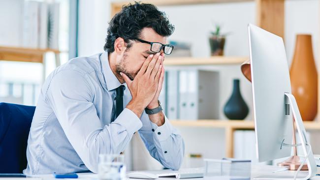 Shot of a young businessman looking stressed out while working on a computer in an office. High functioning anxiety