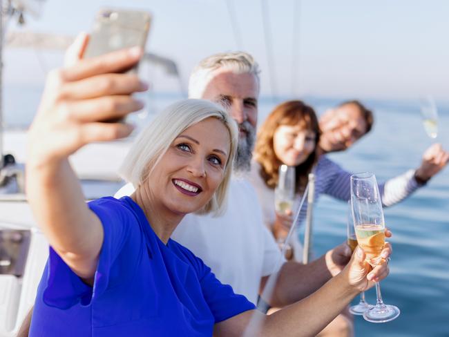 Smiling group of friends traveling on a yacht and drinking champagne. Mature adult friends sitting on sailboat's deck and drinking champagne enjoying the view