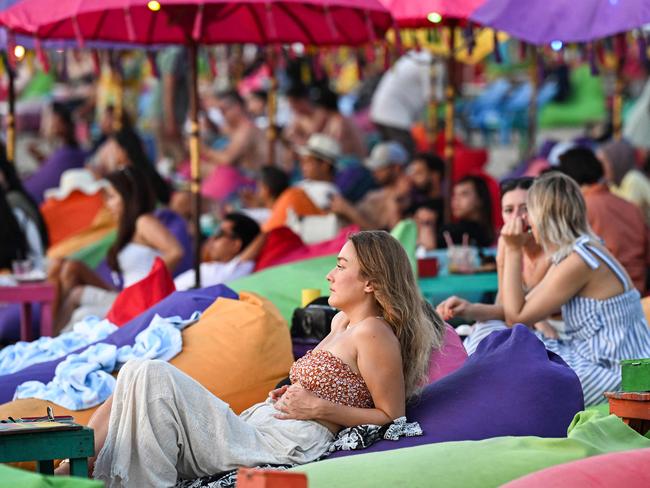 Foreign tourists relax on the Kuta Beach near Denpasar on Indonesia's resort island of Bali on November 18, 2023. (Photo by SONNY TUMBELAKA / AFP)