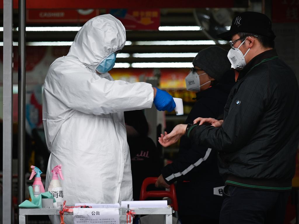 Supermarket staff member wearing a protective suit uses a thermometer to check a customer’s temperature in Beijing Picture: STR.