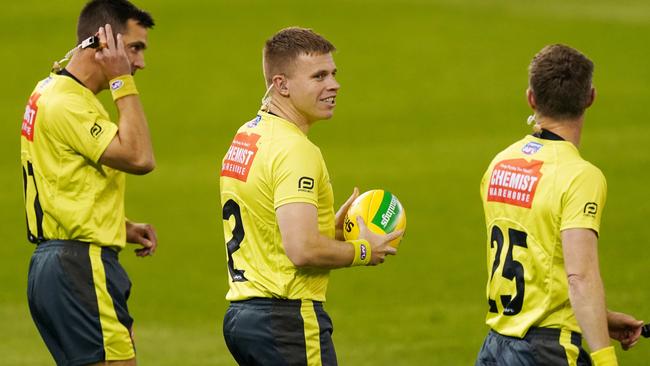 Three umpires walk out to officiate an AFL game. The league plans to increase the number to four.