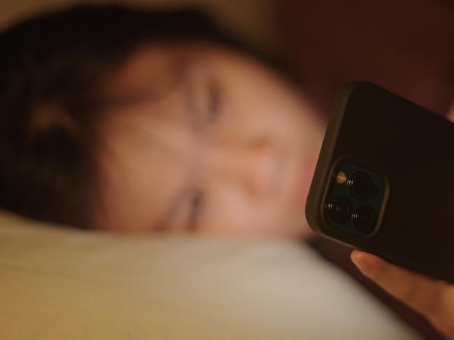 Asian young girl using smartphone on bed at night.