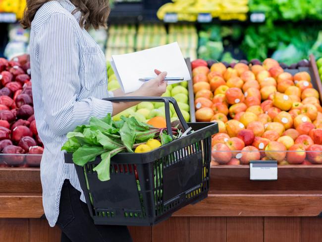 Young woman carries a shopping basket filled with fresh produce. She is shopping for fresh fruit and vegetables in a grocery store.