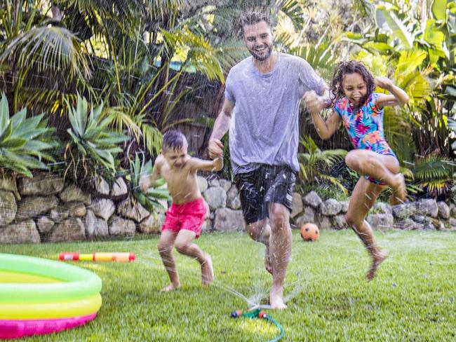 Father and children jumping in sprinkler in the backyard