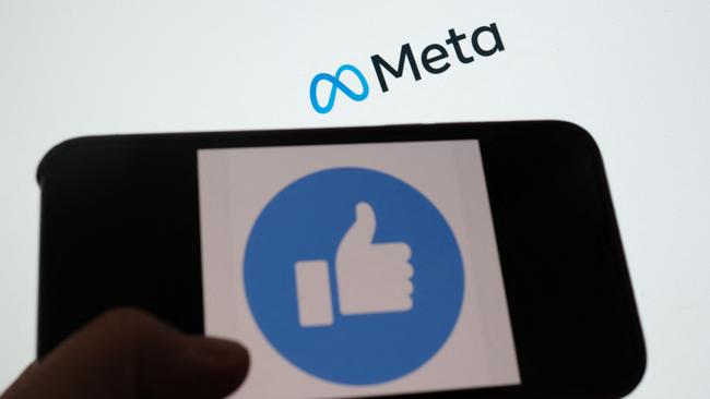 A person using Facebook on a smartphone in front of a computer screen showing the META logo.