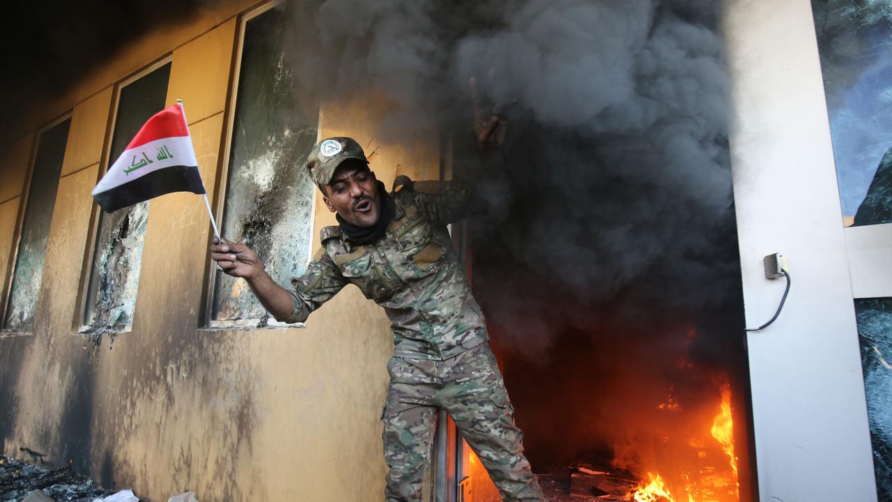 A member of Iraq's Hashed al-Shaabi military network waves a national flag as he exits a burning room after breaching the outer wall of the US diplomatic mission in Baghdad. Picture: Ahmad Al-Rubaye/AFP