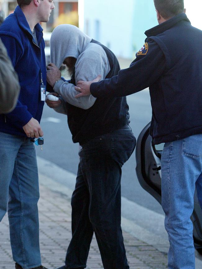 David John Wright hides his face as he is taken to the Burnie Supreme Court in 2004.