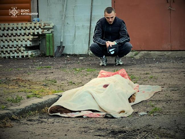 A man squatting next to a covered body following drone attacks on the Kyiv region, amid Russian invasion in Ukraine. Picture: Ukrainian State Emergency Service / AFP
