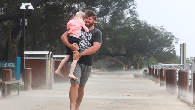 A young boy hides behind his dad as sand flies with the wind. Picture Glenn Hampson