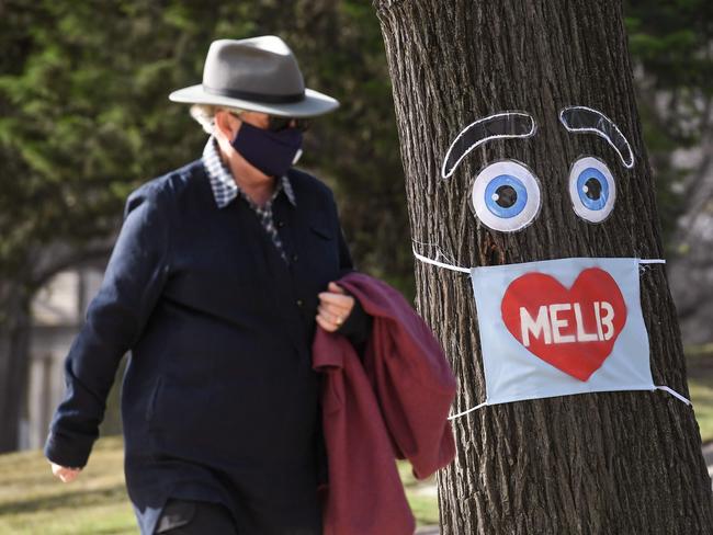 A man walks past a large face mask pinned to a tree in Melbourne on August 3, 2020 after the state announced new restrictions as the city battles fresh outbreaks of the COVID-19 coronavirus. - lia's Victoria state imposed fresh, sweeping restrictions on August 2, 2020, including a curfew in Melbourne for the next six weeks, a ban on weddings, and schools and universities going back online in the coming days. (Photo by William WEST / AFP)