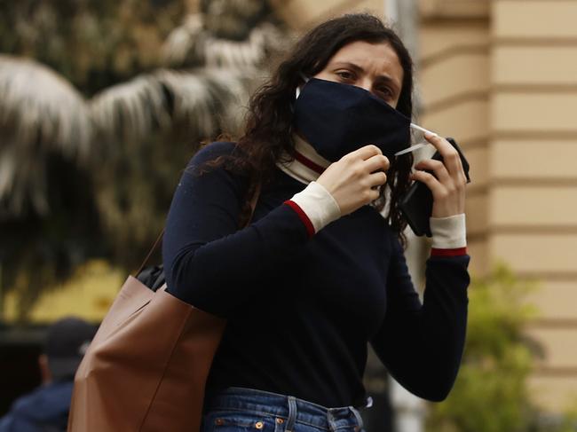 MELBOURNE, AUSTRALIA - NOVEMBER 23: A woman puts on a face mask as she crosses Flinders Street on November 23, 2020 in Melbourne, Australia. COVID-19 restrictions have relaxed further in Victoria as the state continues to record no new coronavirus cases. From Monday, Victorians no longer need to wear masks when outside at all times, with people only required to wear masks when indoors and on public transport, or in places outside where social distancing is not possible. Under the relaxed rules, people will also be allowed to have up to 15 people in their home each day while public gatherings of up to 50 people are permitted outdoors. Capacity limits for cafes, bars and restaurants, along with gyms, indoor sporting venues, cinemas and indoor entertainment along with community venues have also increased. (Photo by Daniel Pockett/Getty Images)