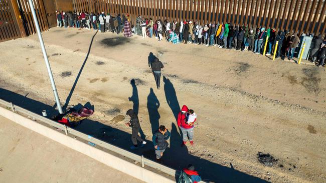 Immigrants line up next to the U.S.-Mexico border fence after spending the night outside.