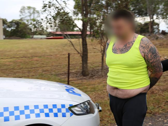 A Rebels bikie gang member being led out of his home in an unflattering yellow singlet.