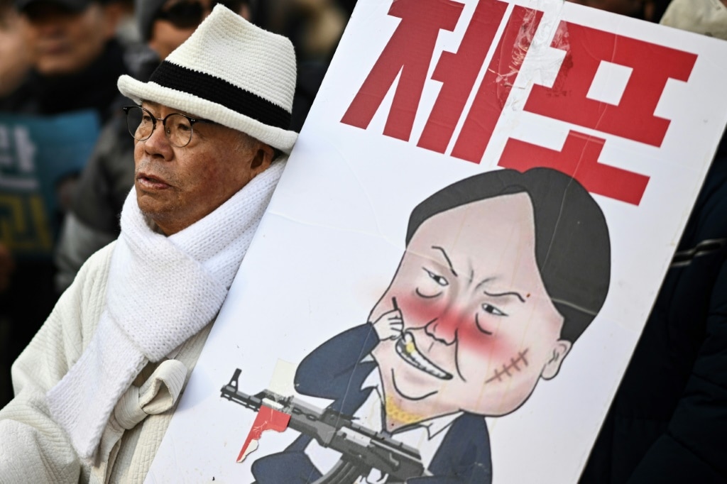 A man carrying a placard with a comic depicting South Korea's impeached president Yoon Suk Yeol