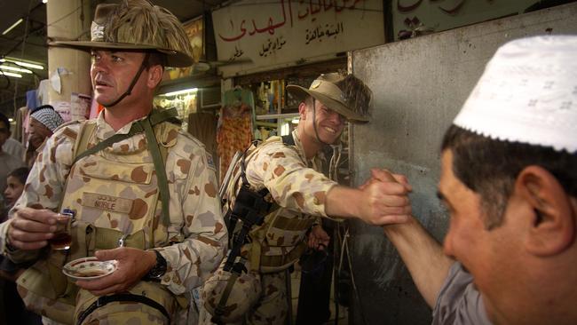 Adjutant to the Al Muthanna Task Group, Captain Angus Hindmarsh shakes the hand of a local while the Commanding Officer, Lieutenant Colonel Roger Noble, now Major General, shares a drink during a visit to the As Samawah souk, Iraq, in 2005.