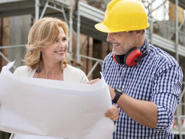 Portrait Of Happy Mature Woman And Male Architect Discussing Plan On Blueprint At Construction Site