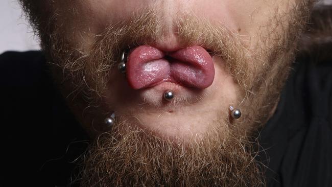 Close-up portrait of man with piercing showing his tongue cut in two