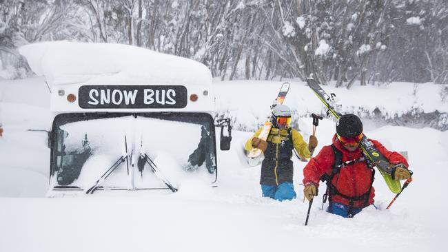 Skiers Buff Farnell and Drew Jolowicz walk past the snow bus at Hotham Alpine Resort as the big storm system continues to sweep through the Alps. Picture: Dylan Robinson