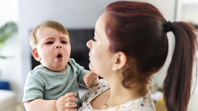 A mother holding child baby on the living room. The baby is sick having some cough. Istock Photo